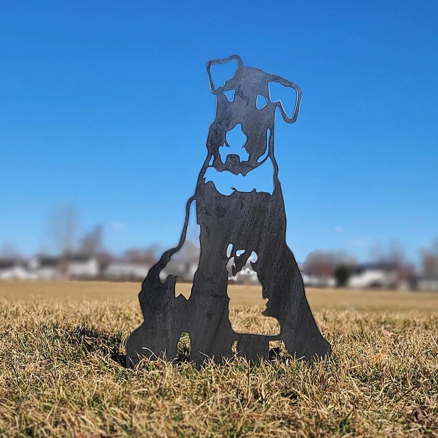 Airedale Terrier metal silhouette in matte black, standing on grassy ground against a clear blue sky.