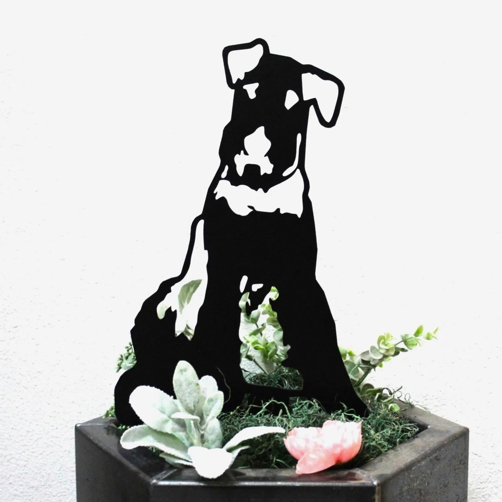 Black Airedale Terrier metal silhouette displayed among faux greenery in a planter, showcasing its detailed design.