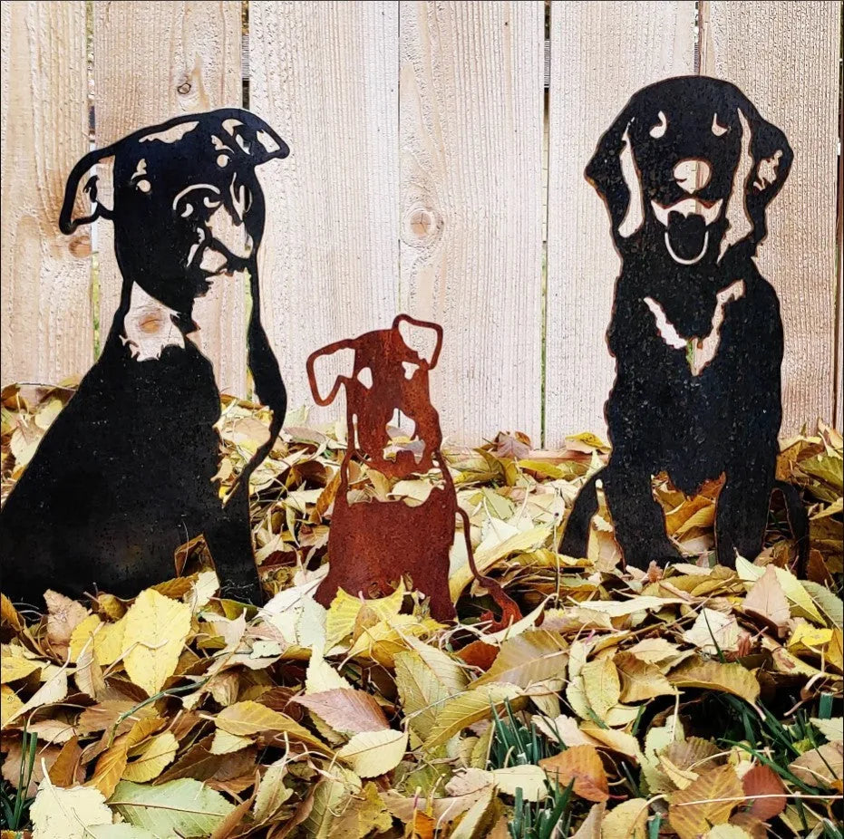 Airedale Terrier metal silhouettes, one rusted and two black, resting among colorful autumn leaves.