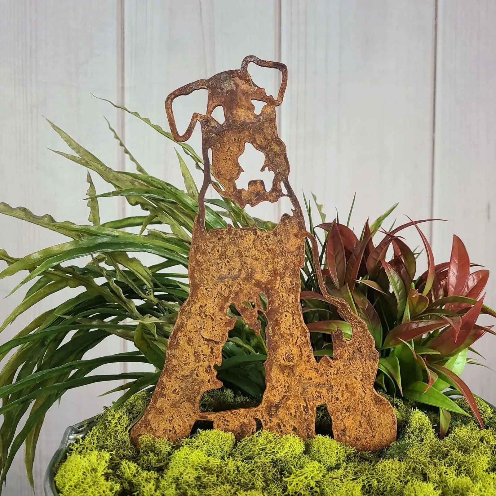 Airedale Terrier metal silhouette in rusted Corten steel, surrounded by lush greenery and moss.