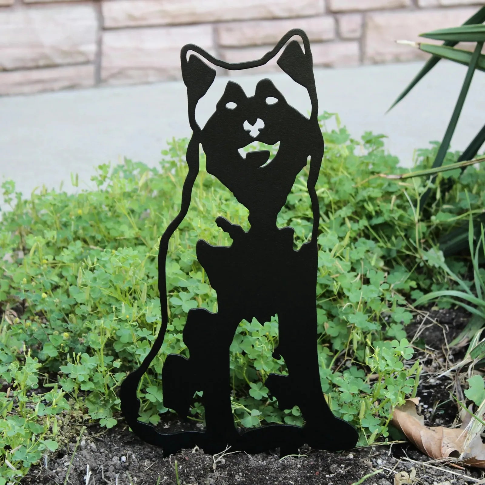 Black metal silhouette of an Alaskan Malamute standing in green foliage, ideal for outdoor dog decor.
