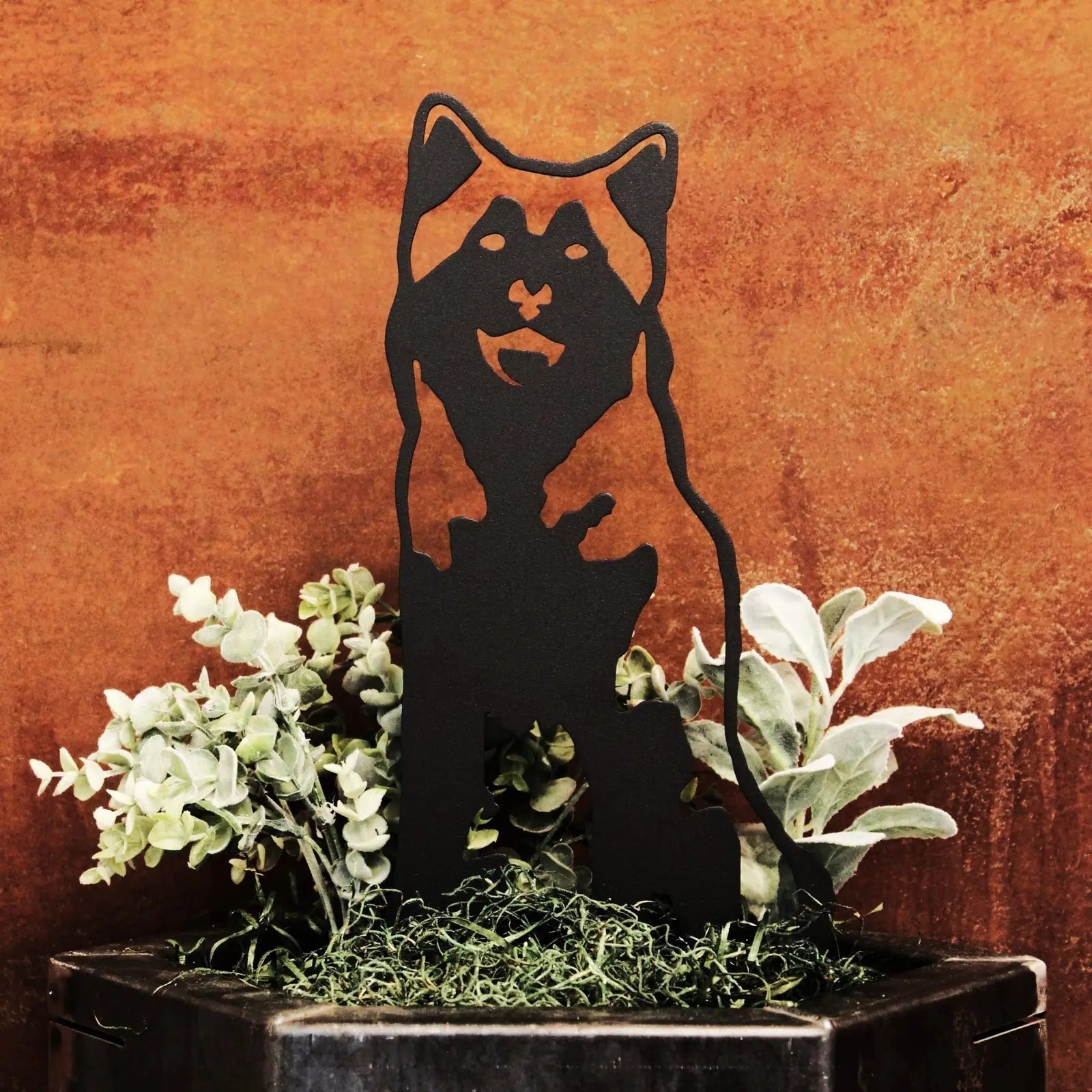 Black metal silhouette of an Alaskan Malamute, set among greenery, showcasing a rustic outdoor decor style.