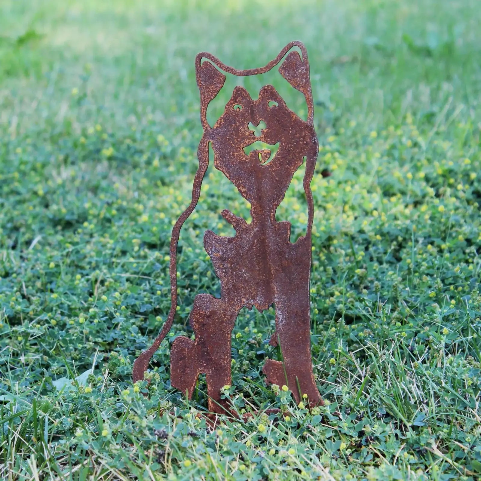 Rusty Corten steel silhouette of an Alaskan Malamute, showcasing intricate detail, set in lush green grass.