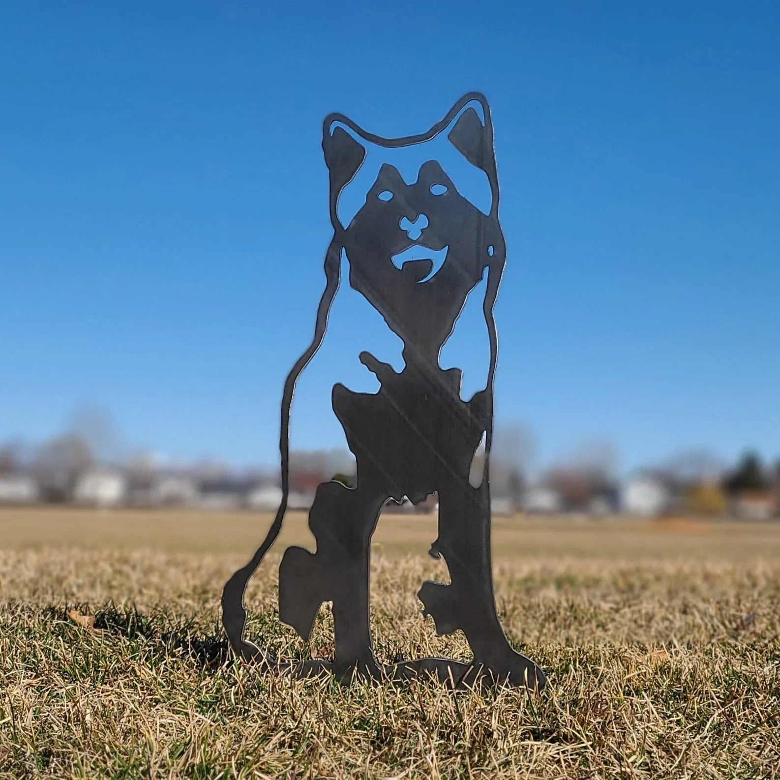 Alaskan Malamute metal silhouette in black, displayed on grass against a clear blue sky, adding rustic outdoor decor.