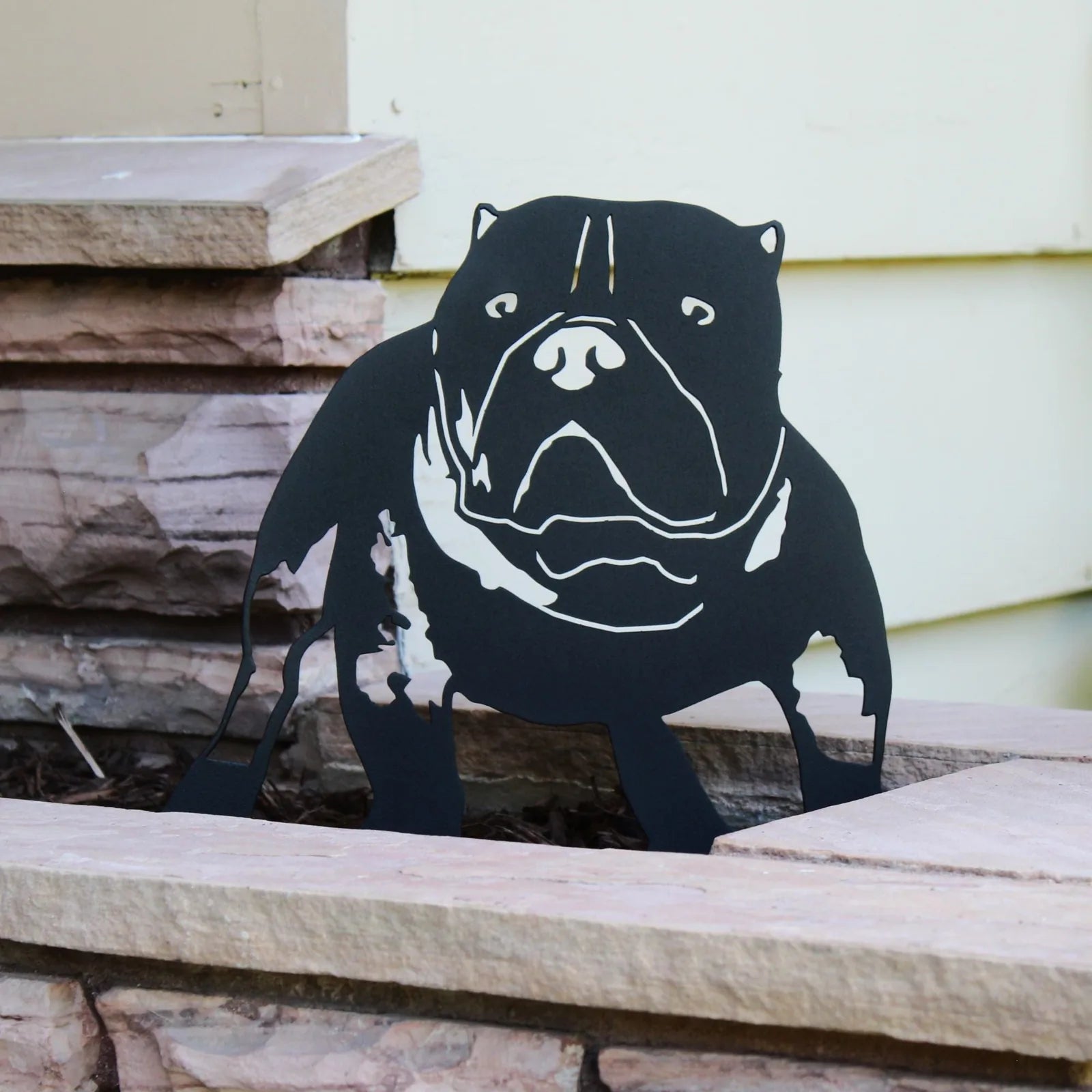 Black silhouette of an American Bully metal wall art leaning on a stone ledge, showcasing detailed features and craftsmans...