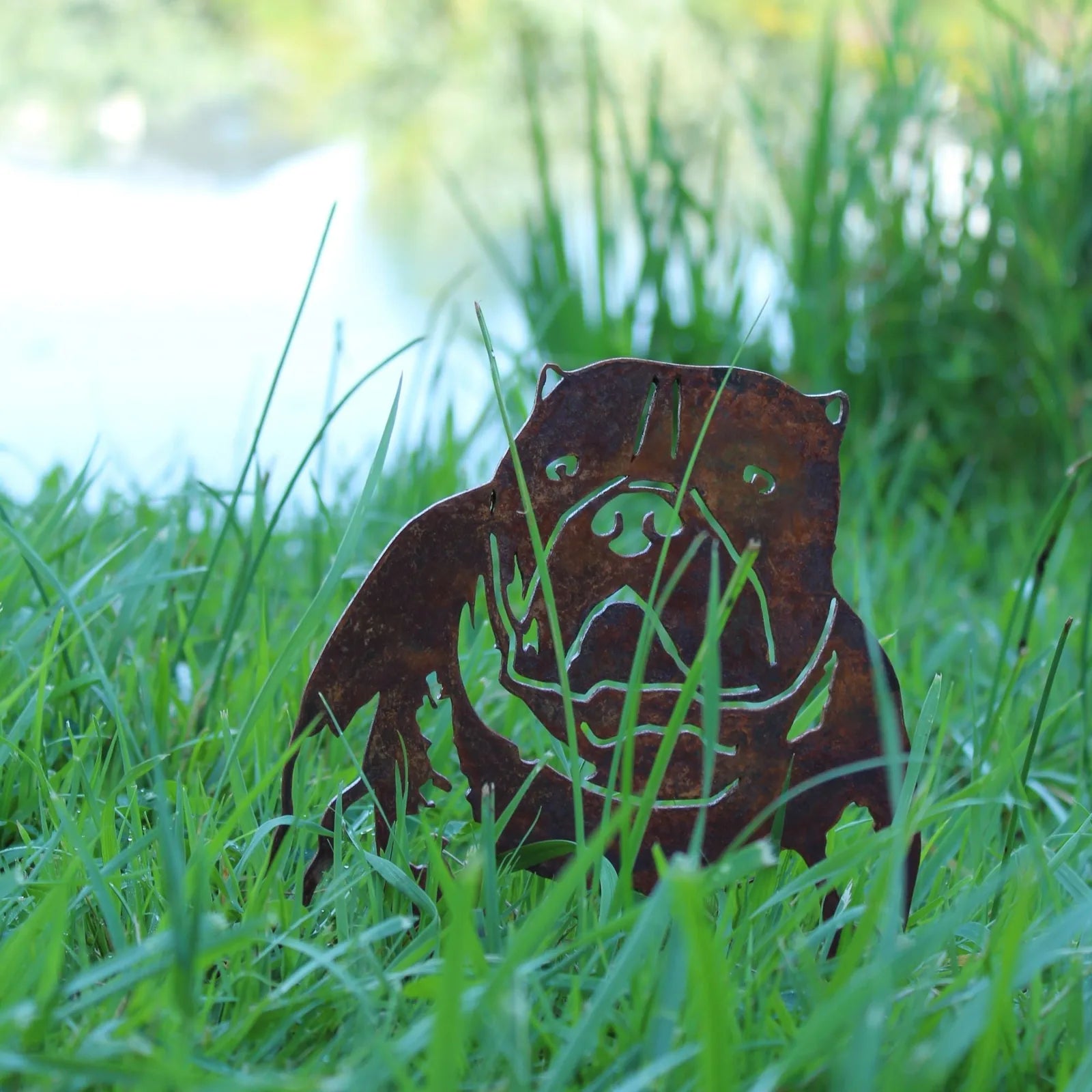 Rusty Corten steel silhouette of an American Bully dog, nestled among tall green grass by a serene background.