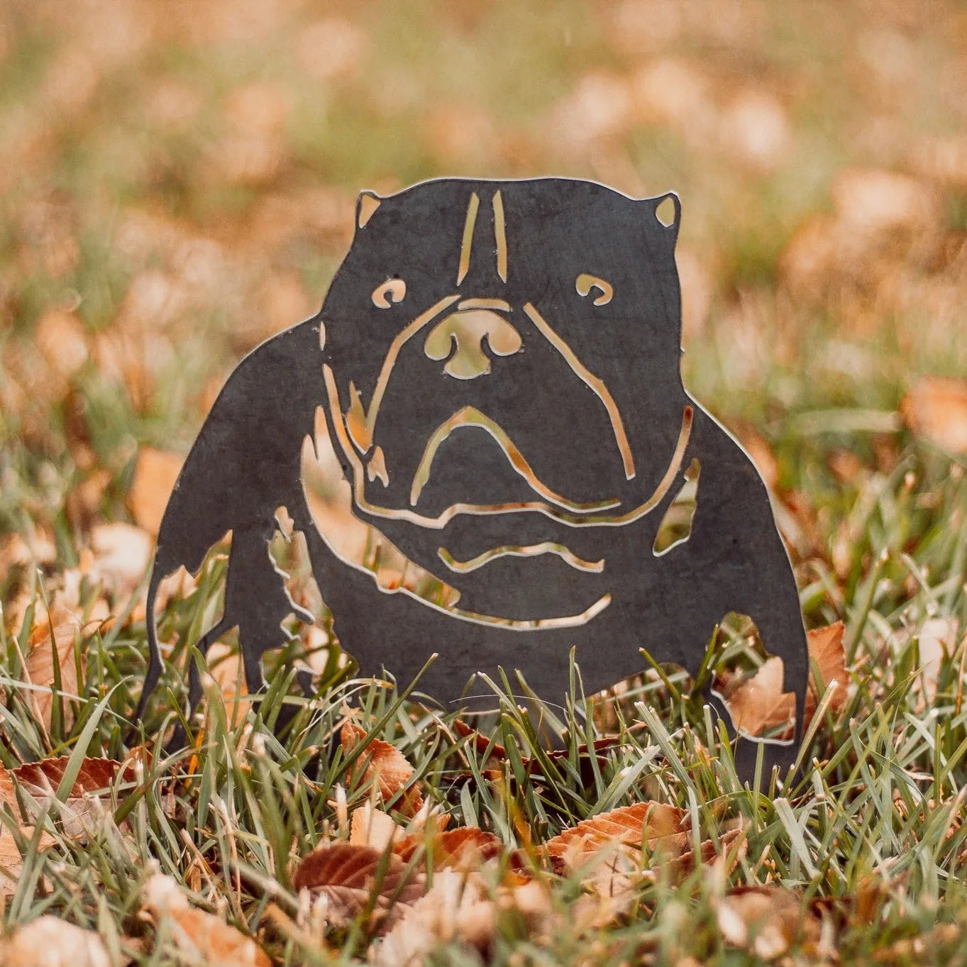 American Bully silhouette in Corten steel with intricate cutouts, placed on grass amid autumn leaves.