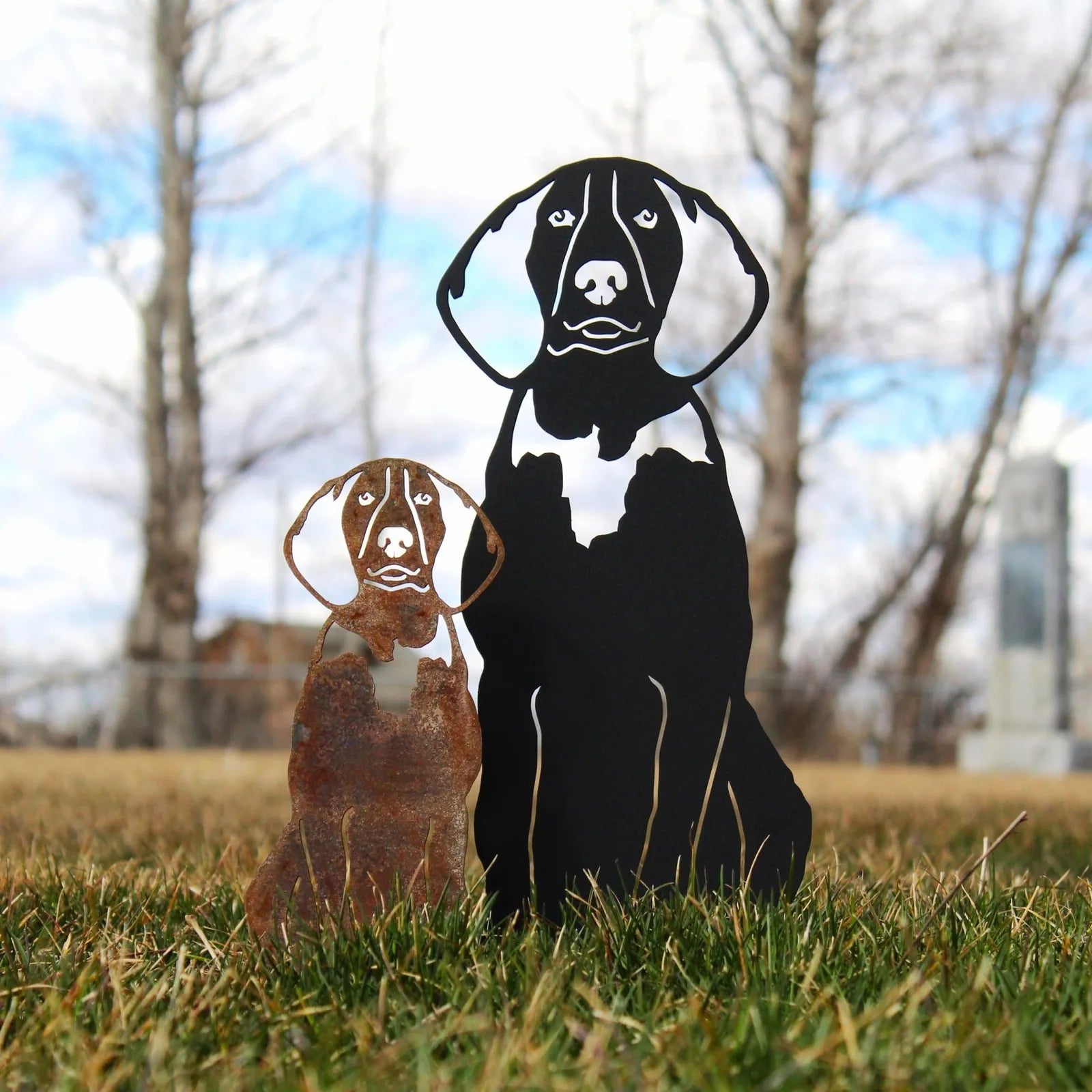 Metal silhouette of American English Coonhounds in Corten steel and black finish, displayed outdoors on grass.