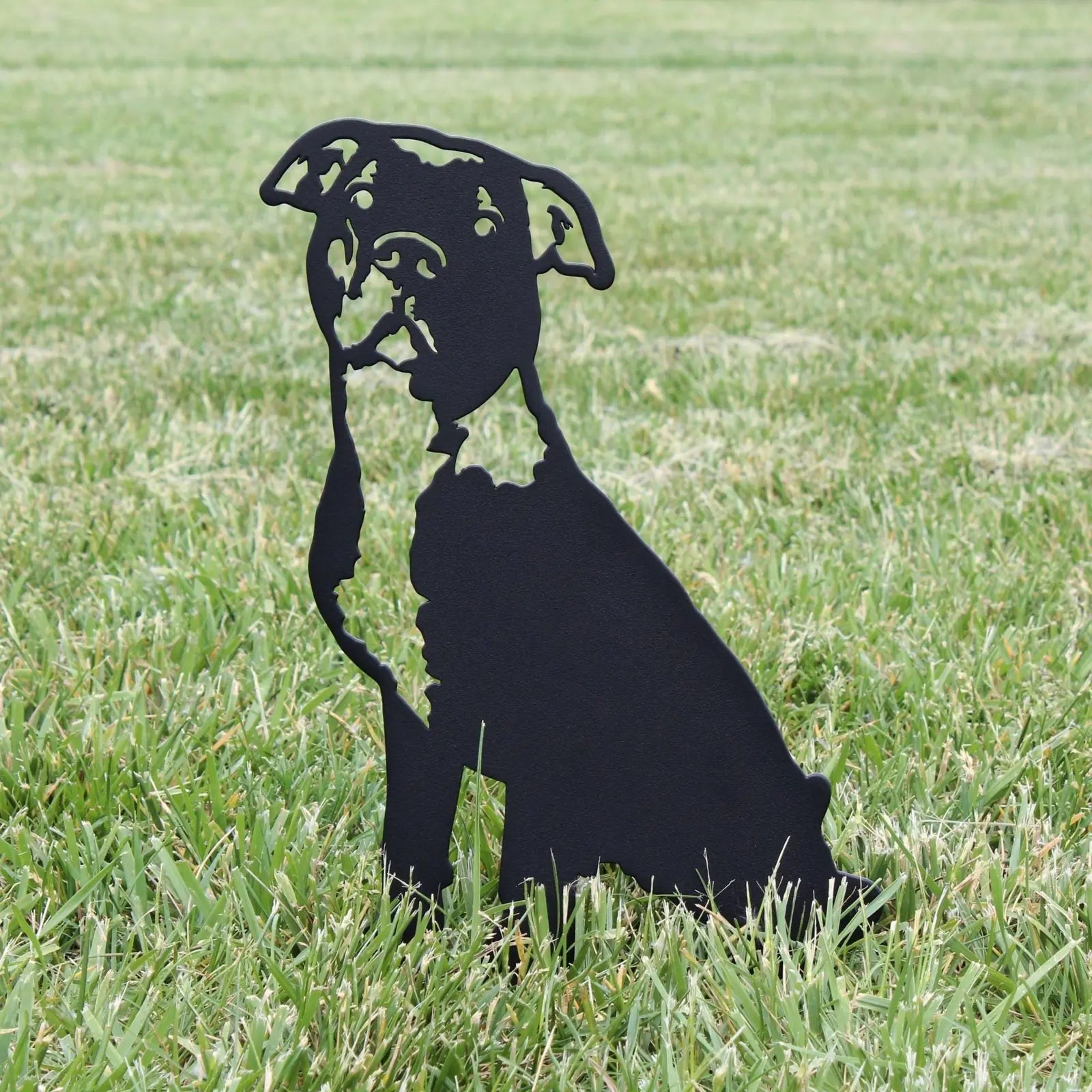 Black metal silhouette of an American Pit Bull Terrier sitting on green grass, showcasing its intricate design.