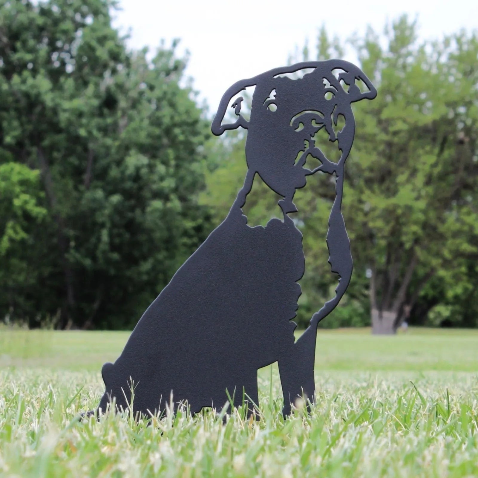 Black metal silhouette of an American Pit Bull Terrier standing in grass, showcasing intricate detailing against a natural...