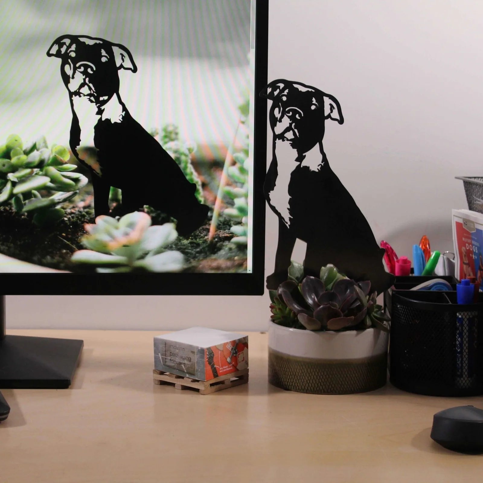 Black metal silhouette of an American Pit Bull Terrier next to plants on a desk, showcasing its elegant outdoor decor design.