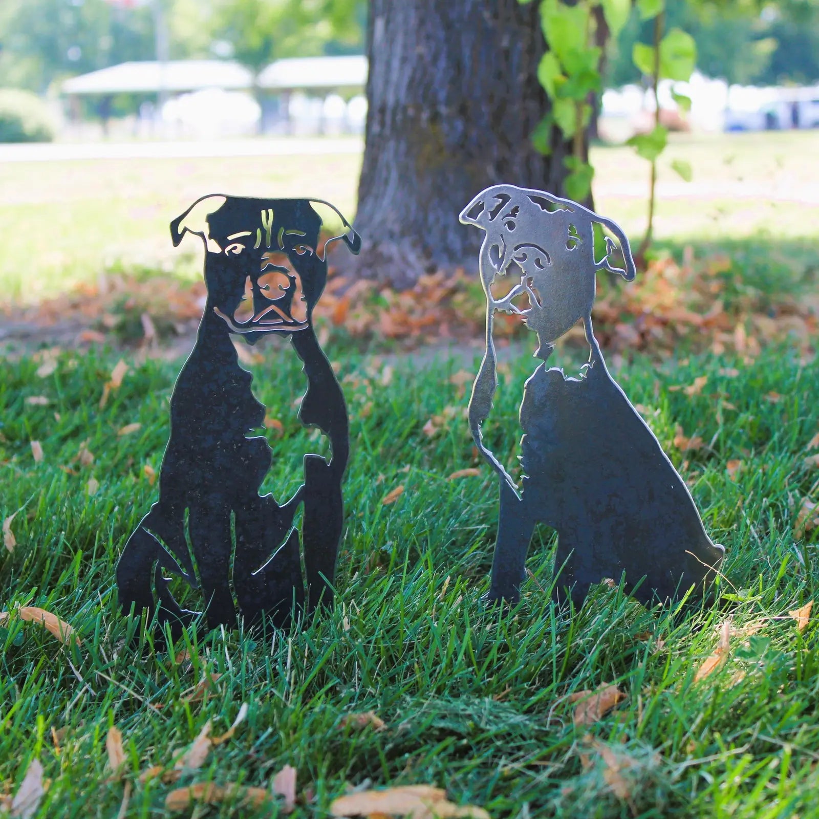 Black metal silhouettes of American Pit Bull Terriers sit on green grass, showcasing their stylish outdoor decor design.