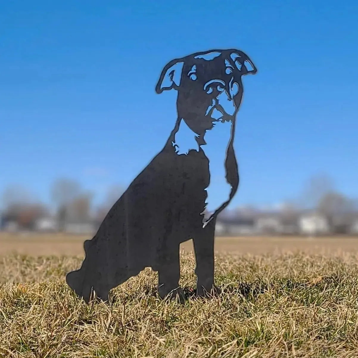 Handmade black metal silhouette of an American Pit Bull Terrier, placed on grass against a blue sky, perfect for outdoor d...