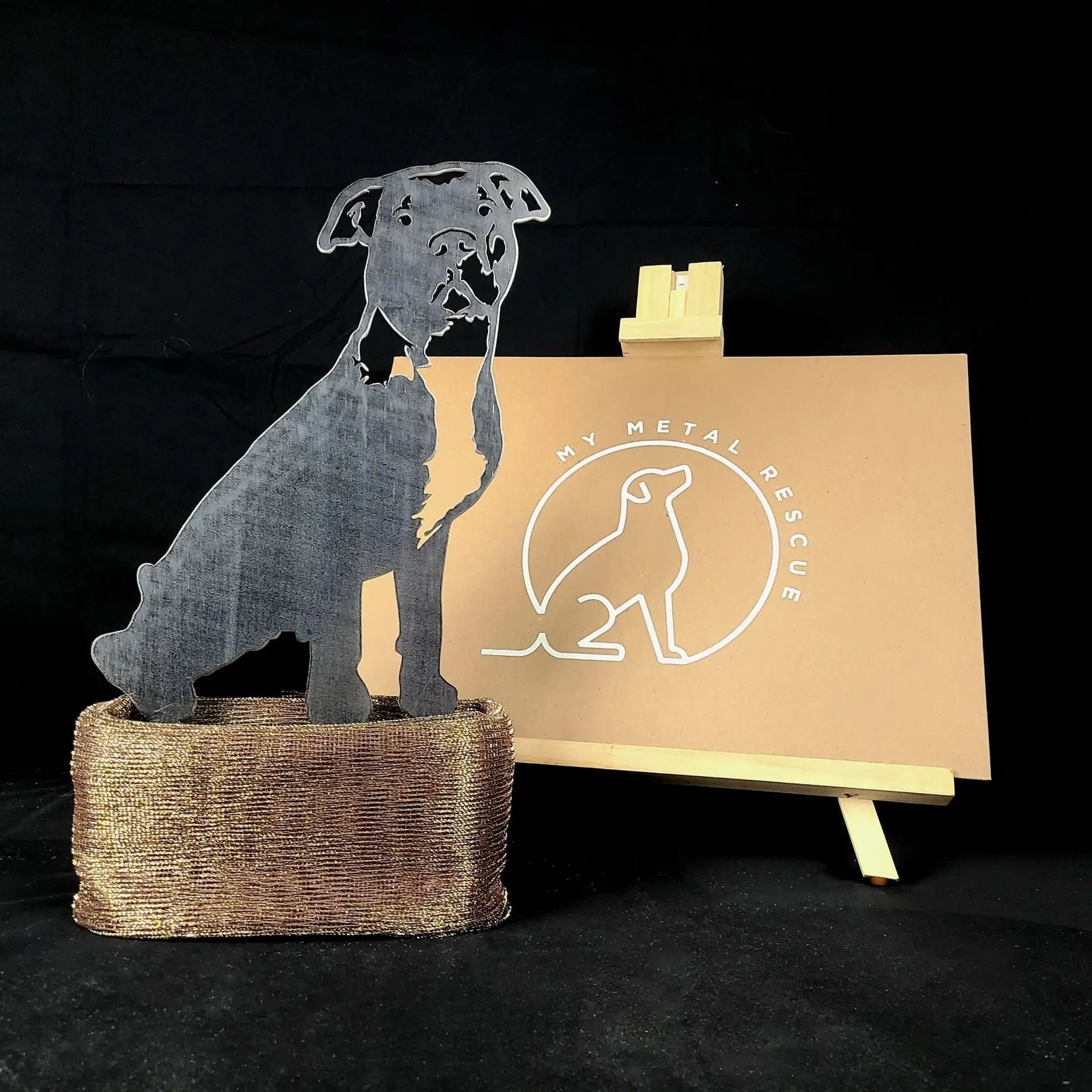 American Pit Bull Terrier metal silhouette in matte black, displayed on a textured gold base with a logo backdrop.
