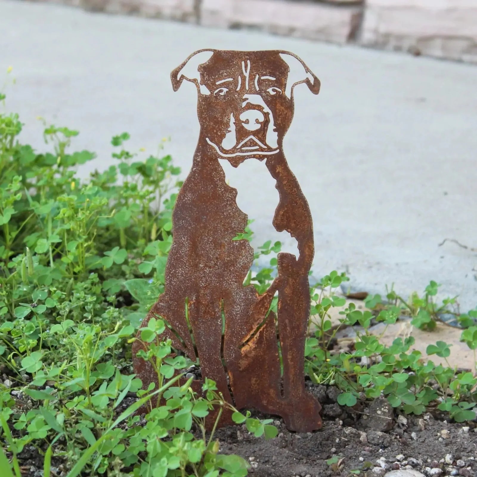 Handcrafted rust-colored metal silhouette of an American Staffordshire Terrier sitting among greenery.