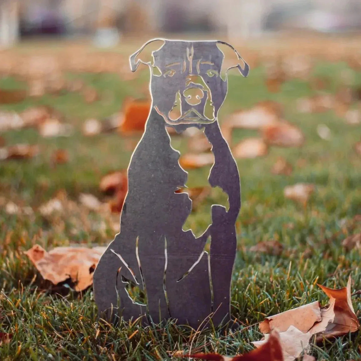 Handcrafted metal silhouette of an American Staffordshire Terrier among fallen leaves on green grass.