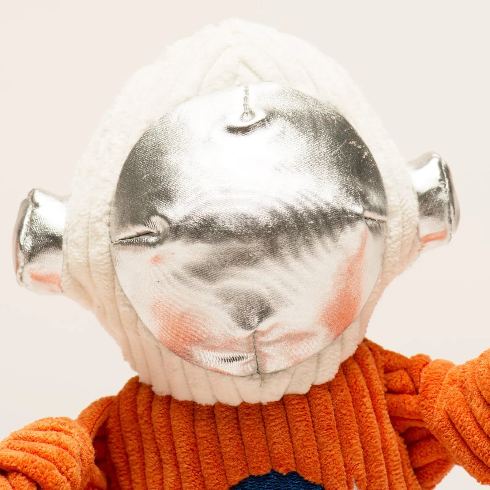 Plush dog toy Astro-Knottie® featuring a silver helmet, orange suit, and textured limbs for interactive play.