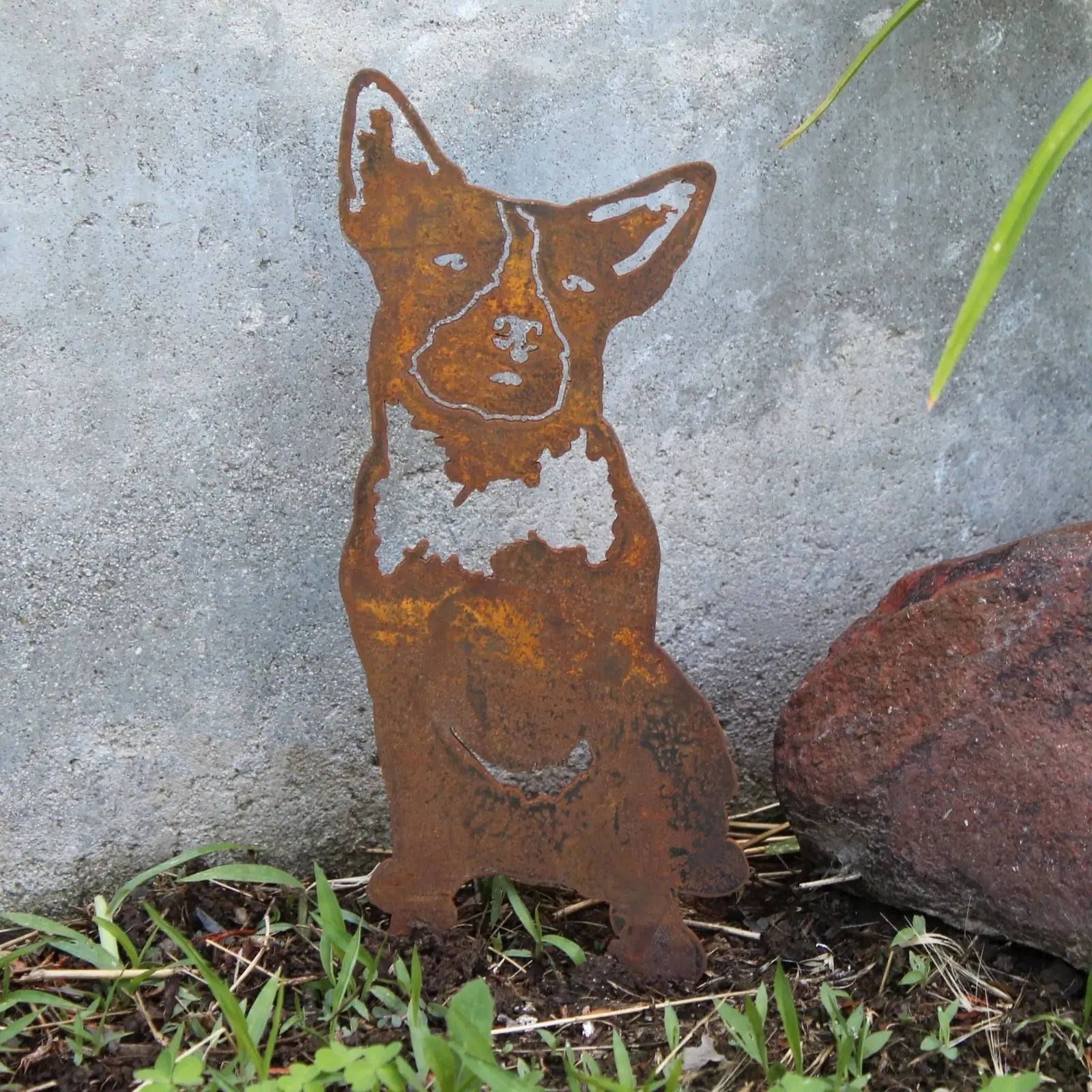 Australian Cattle Dog metal silhouette in rusted Corten steel, positioned outdoors among grass and stones.