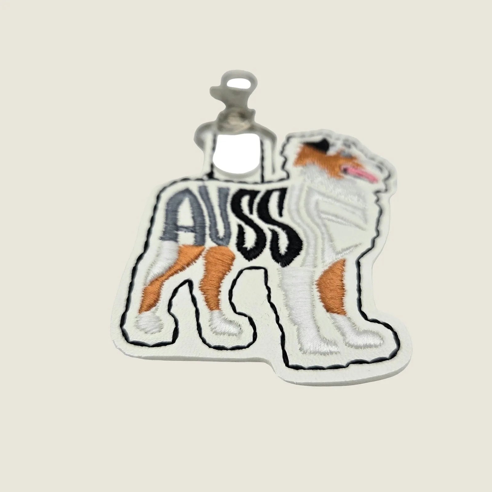 Embroidered Australian Shepherd keychain in tan, white, and black on ivory faux leather with a metal swivel clasp.