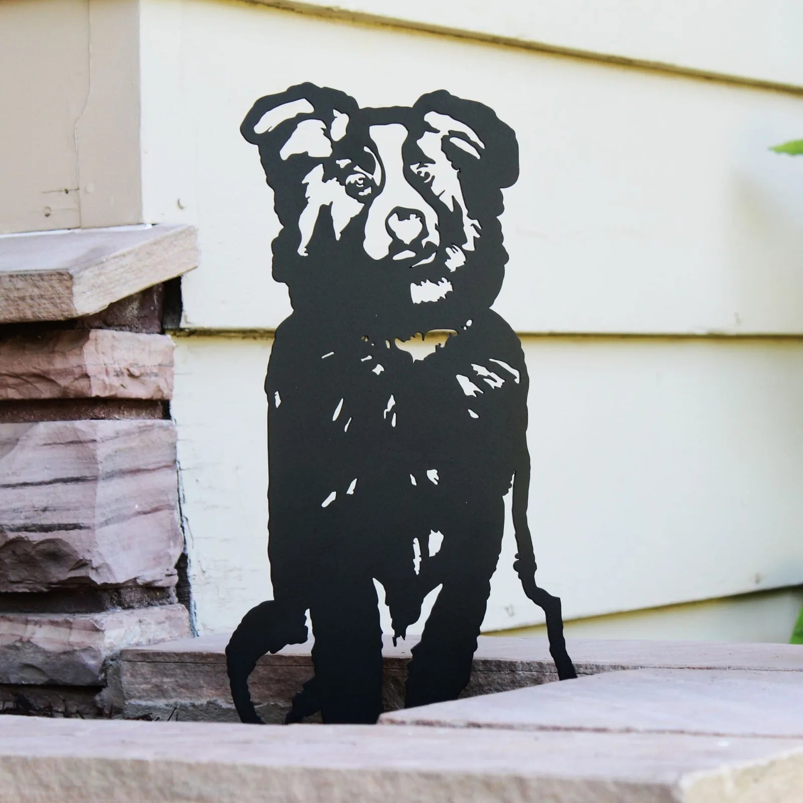 Black metal silhouette of an Australian Shepherd dog standing on stone steps against a light-colored wall.