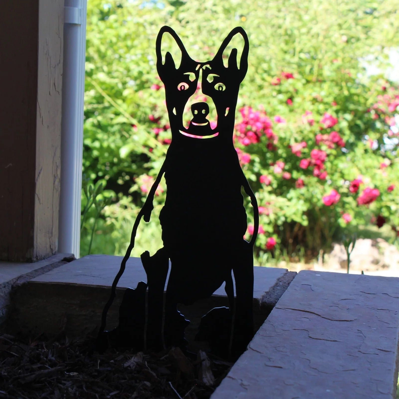 Basenji dog silhouette in matte black metal, set against a garden backdrop with vibrant flowers. Perfect for outdoor decor.