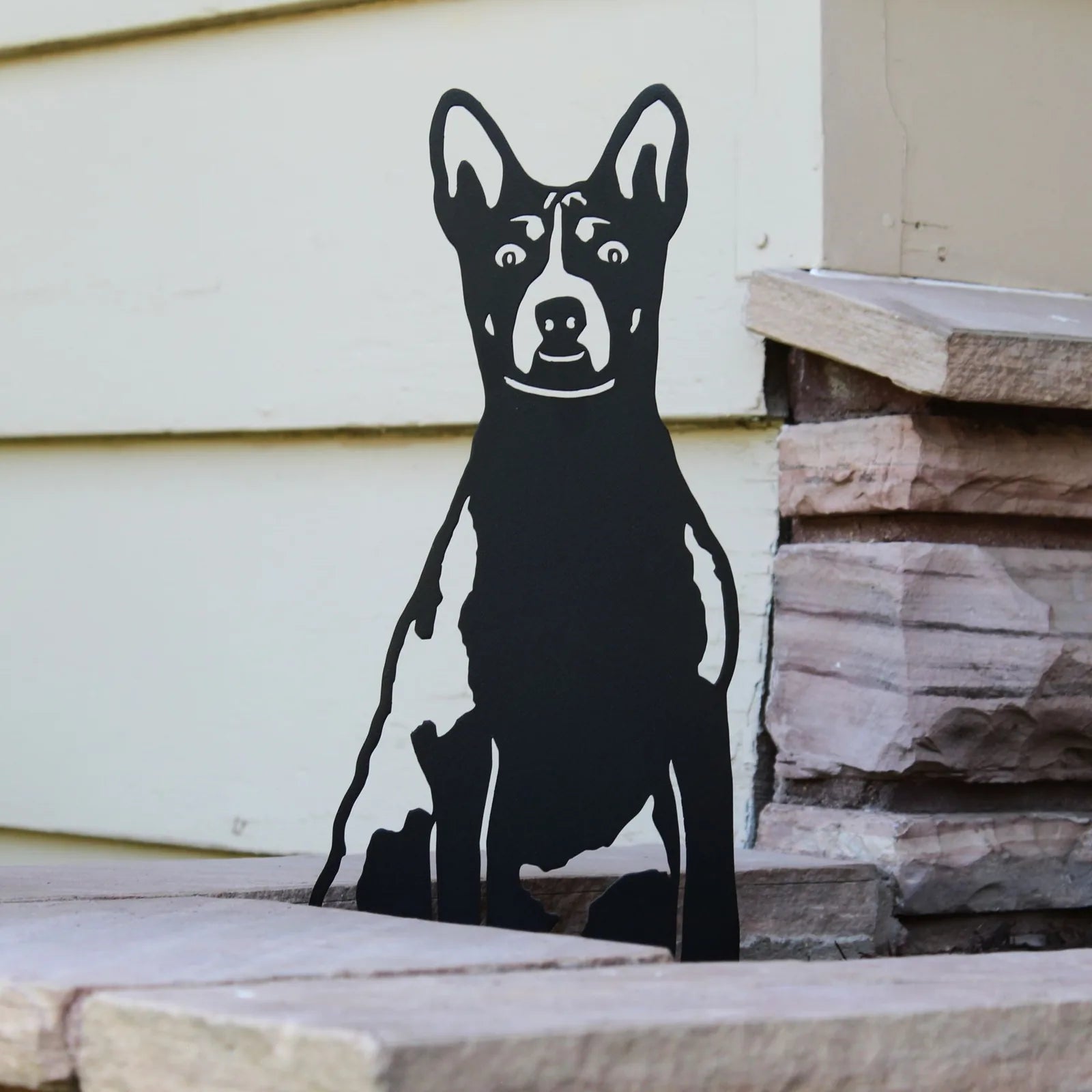 Black Basenji metal silhouette art resting on stone, showcasing detailed cutouts and sturdy design for outdoor decor.