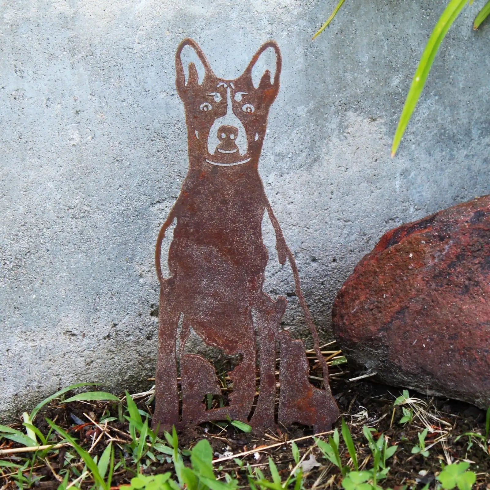 Rusty Basenji metal silhouette standing in grass against a gray wall, adding rustic charm to outdoor decor.