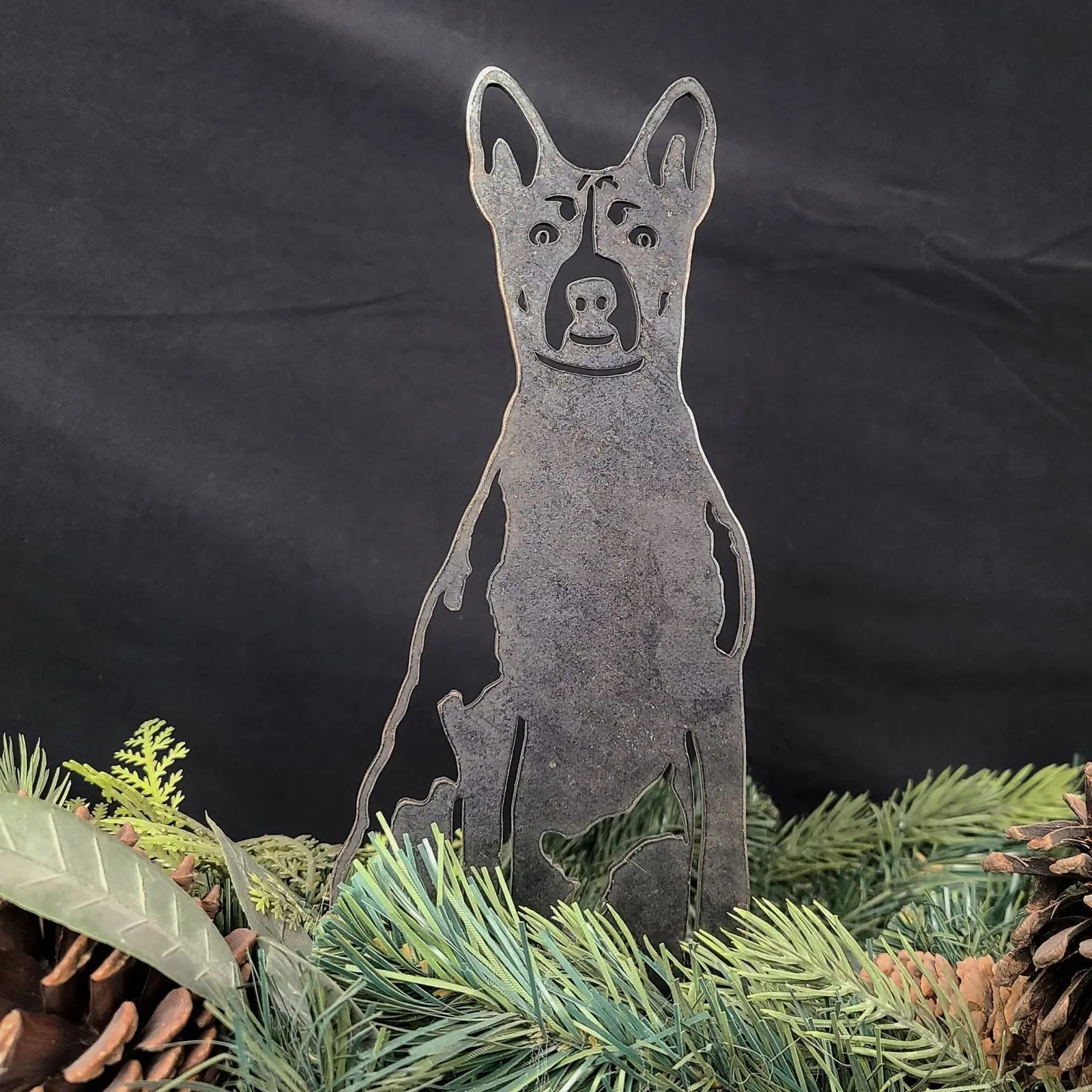 Basenji metal silhouette in rustic finish, surrounded by pine leaves and cones, showcasing outdoor dog decor.