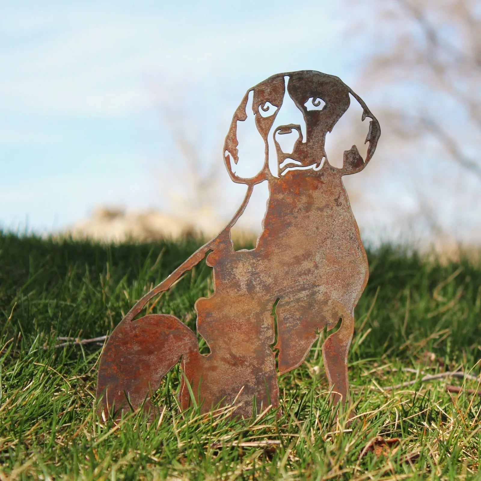Rusty Beagle silhouette sculpture made of Corten steel, set against lush green grass and a clear blue sky background.