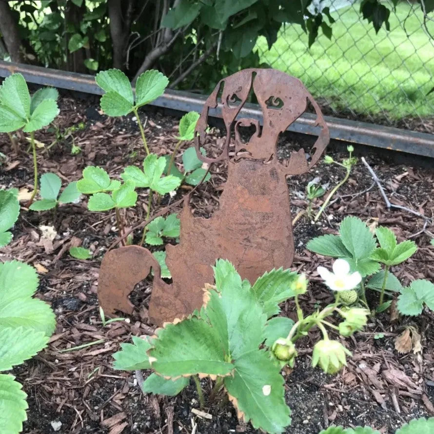 Rusty metal Beagle silhouette accent among green strawberry plants in a garden, adding rustic dog decor charm.