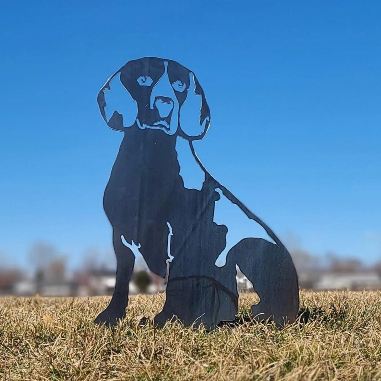 Beagle metal silhouette in matte black, showcasing detailed features against a clear blue sky on grassy ground.