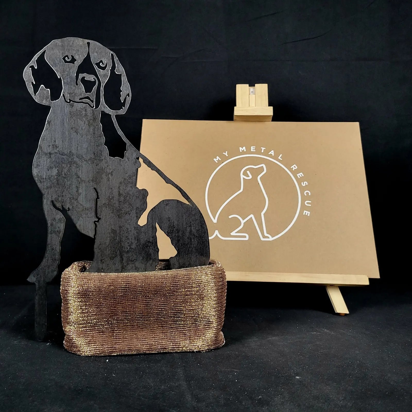 Beagle metal silhouette in matte black resting on a textured bronze base, set against a neutral backdrop.