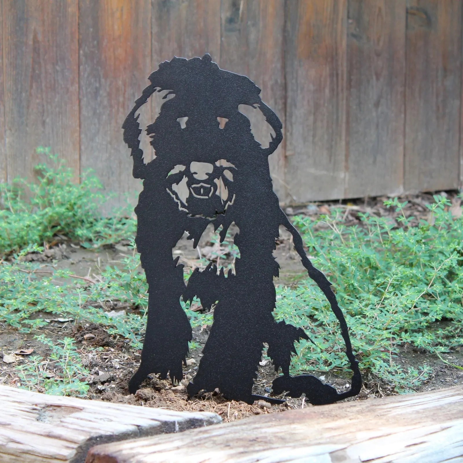 Bearded Collie metal silhouette in matte black against green foliage, adding rustic dog decor to an outdoor space.