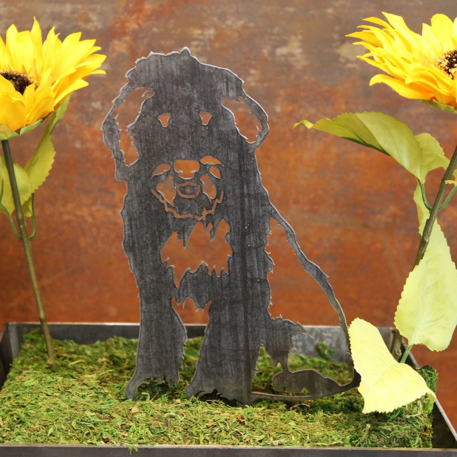 Bearded Collie metal silhouette in black, surrounded by yellow sunflowers and greenery on a rustic backdrop.
