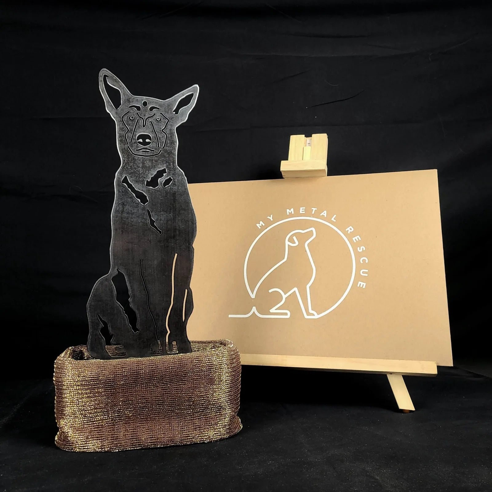 Belgian Malinois metal silhouette in black, displayed on a textured base, with a "My Metal Rescue" sign in the background.