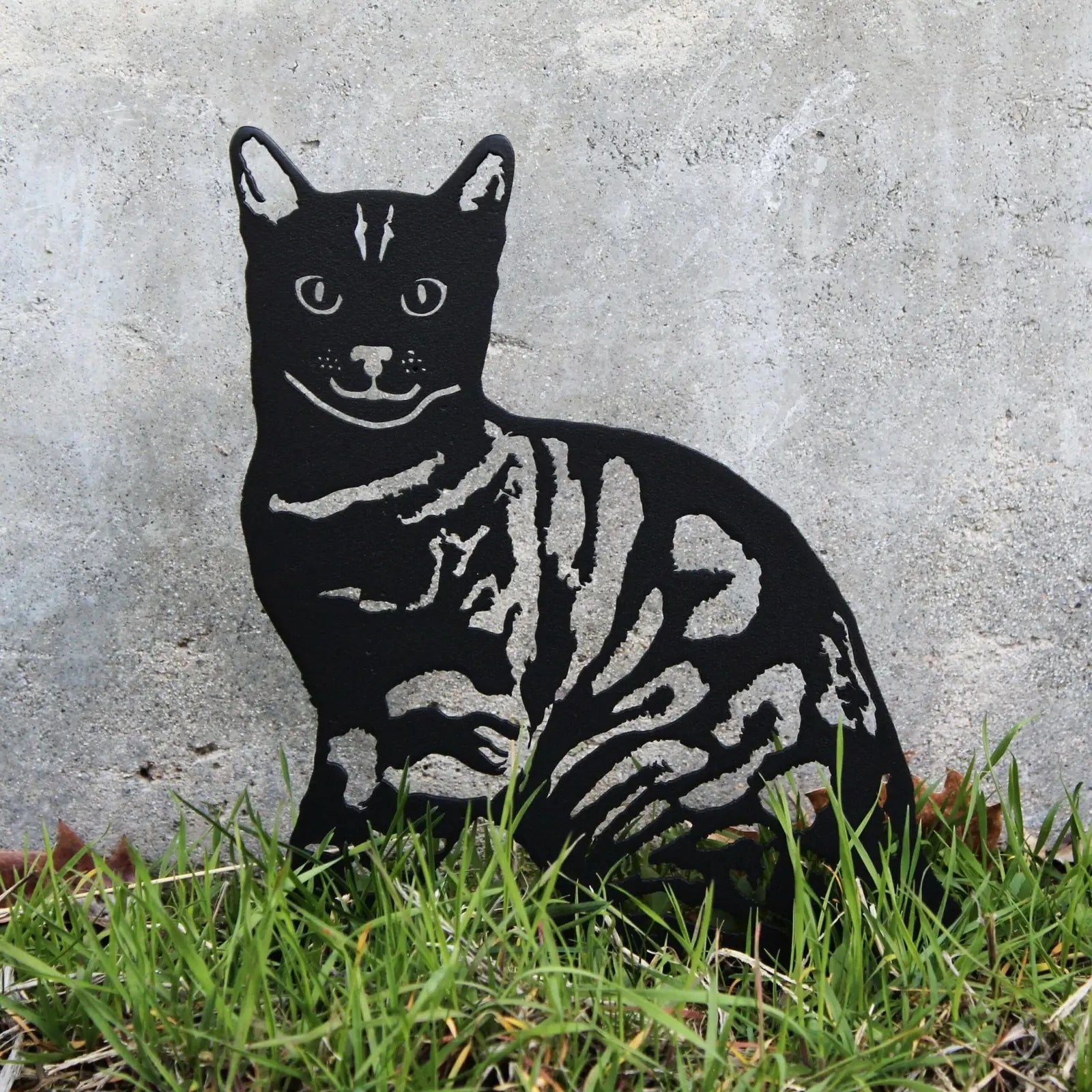 Black metal Bengal cat silhouette with detailed stripes, set against a textured background and surrounded by grass.