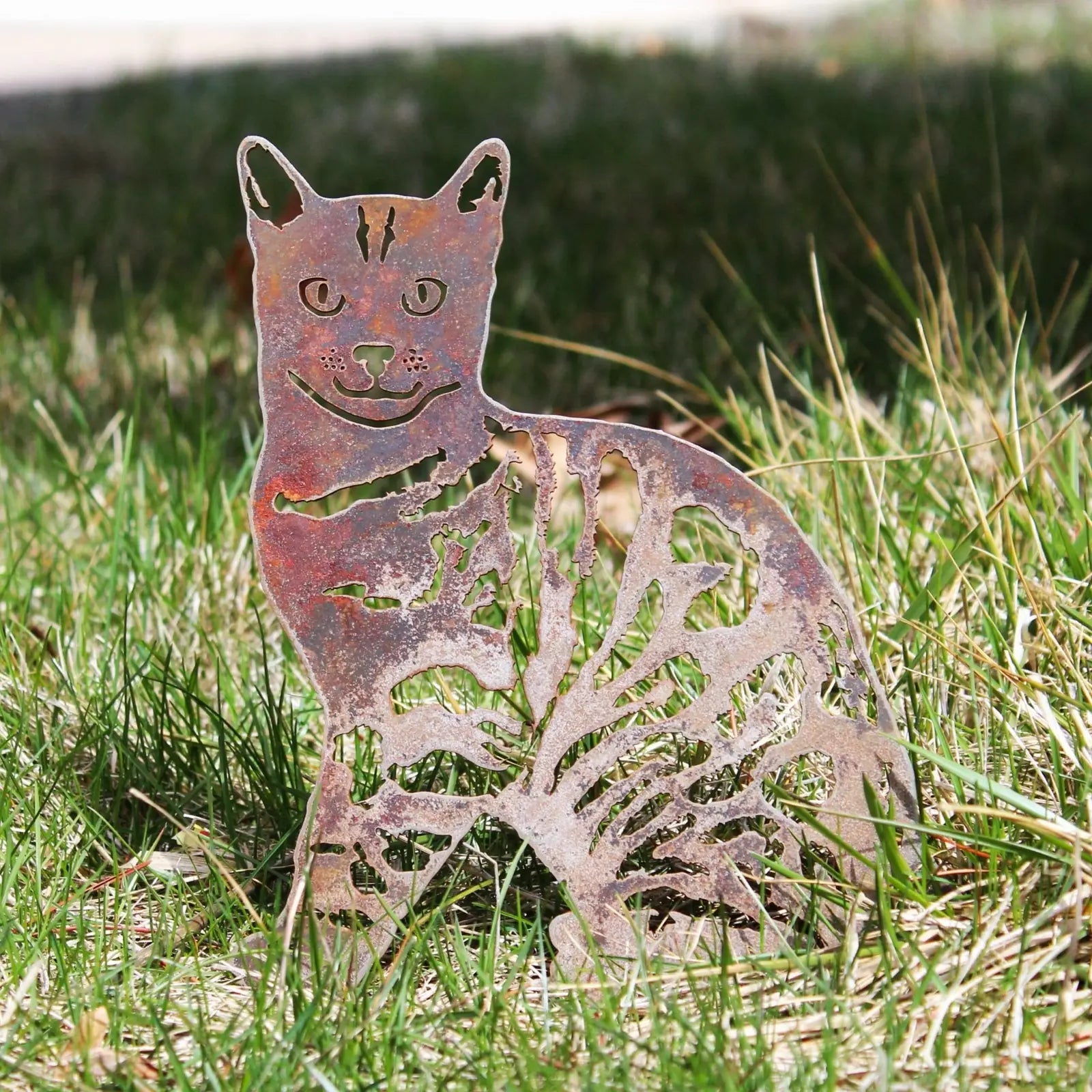 Handmade Bengal metal silhouette in weathered Corten steel, depicting a playful cat design, set against green grass.
