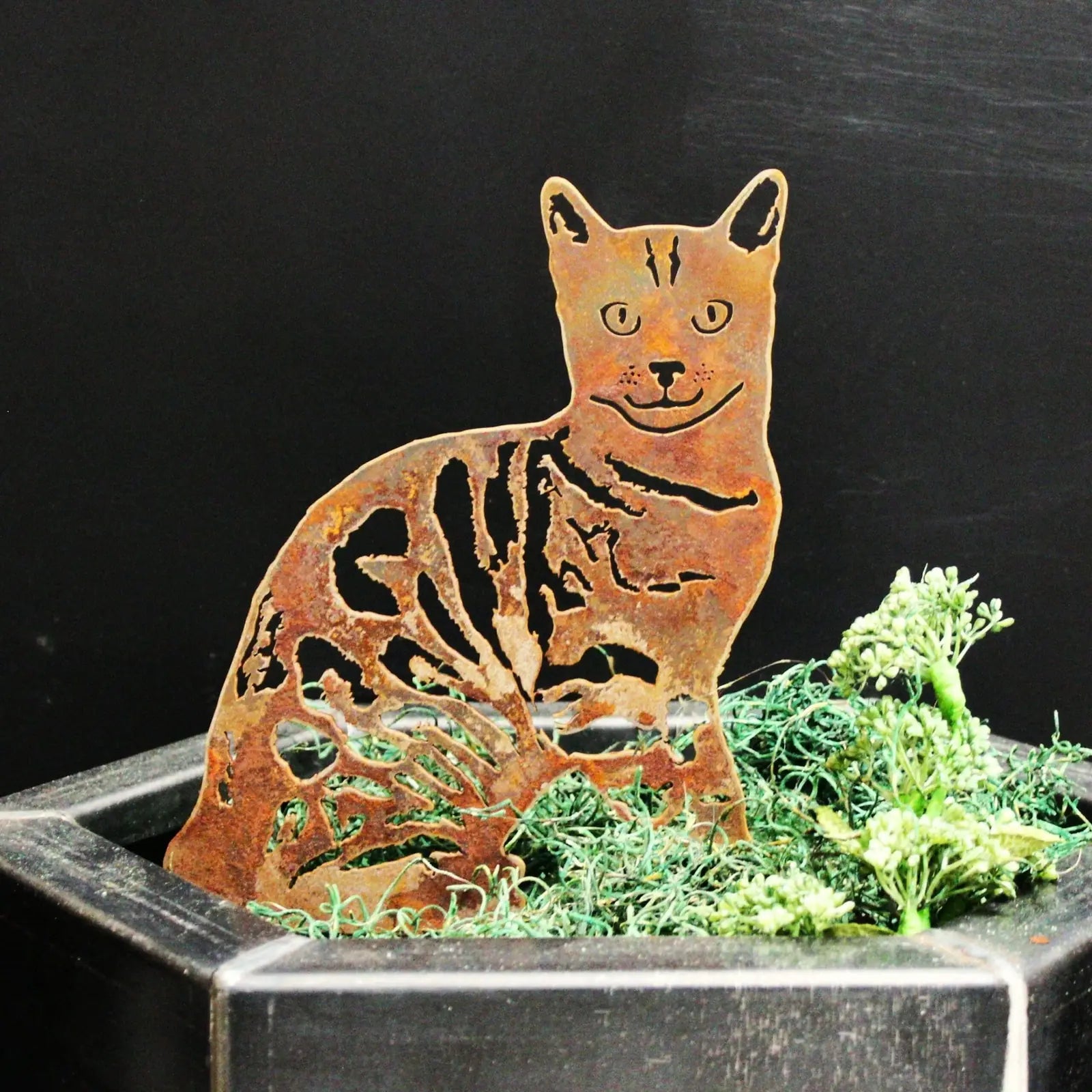 Rusty Bengal metal silhouette art piece sitting on green moss in a black planter, showcasing intricate cutout details.