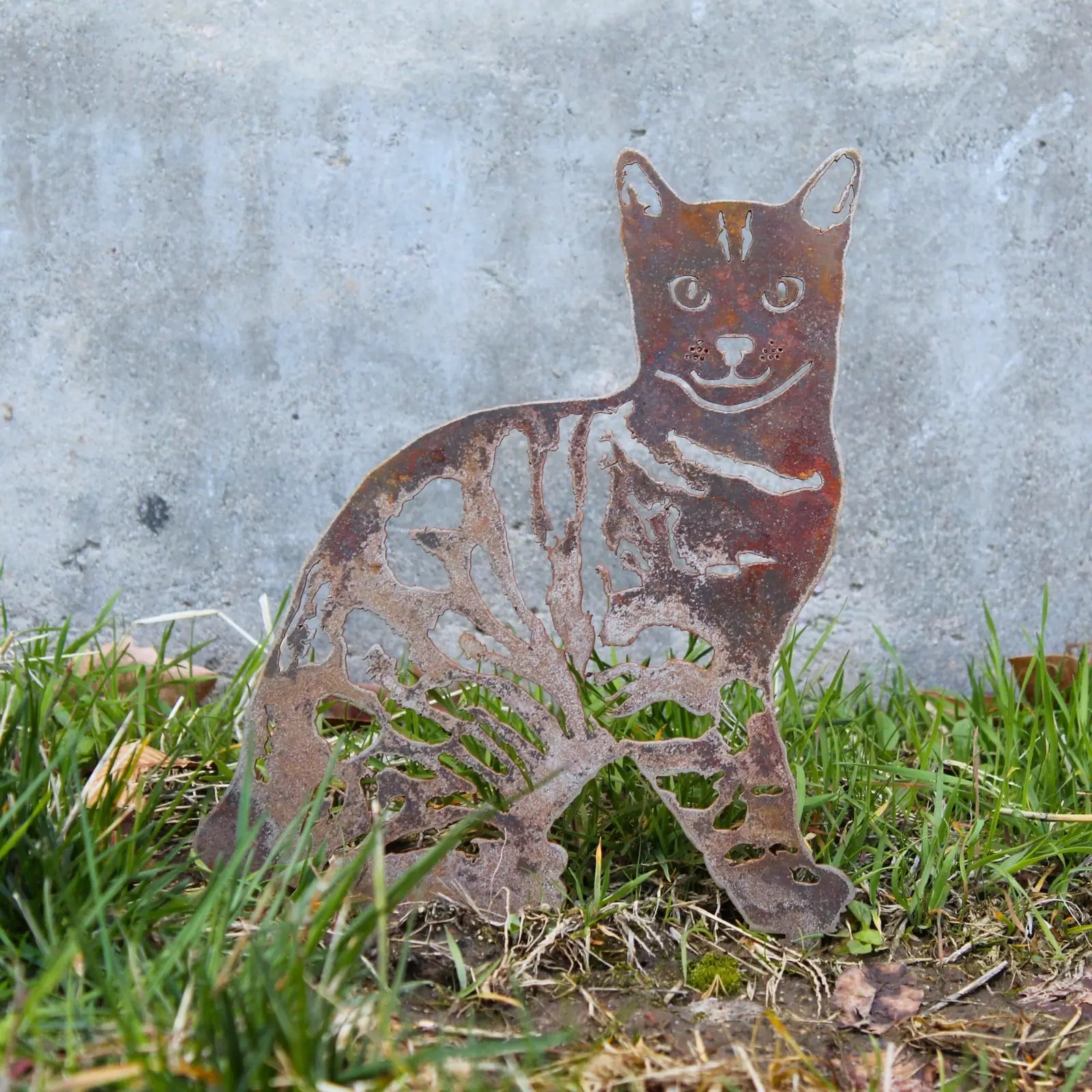 Bengal cat silhouette in rust-colored Corten steel, set against grass and concrete background.
