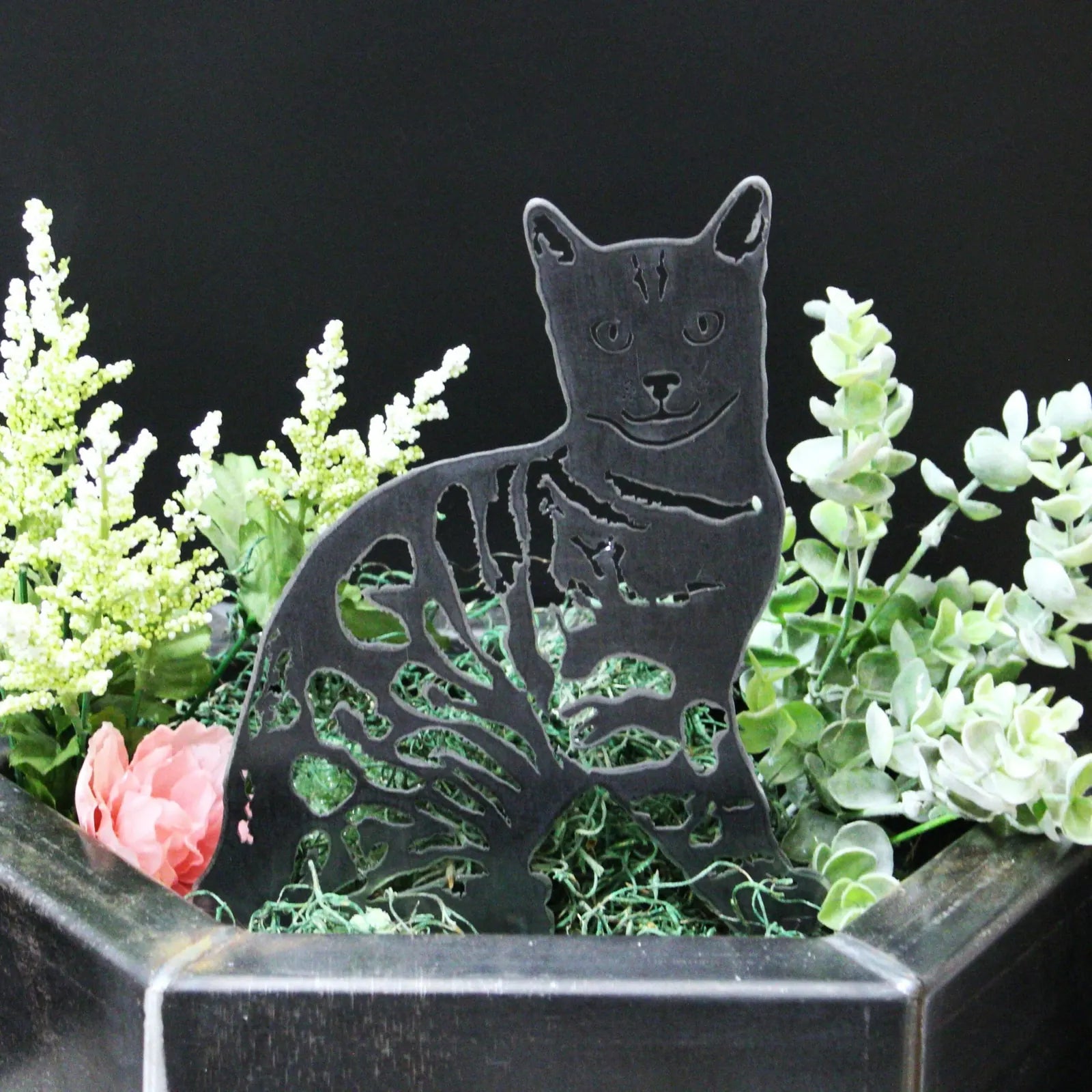 Black Bengal metal silhouette amid greenery and faux flowers, showcasing intricate cut-out design for outdoor decor.