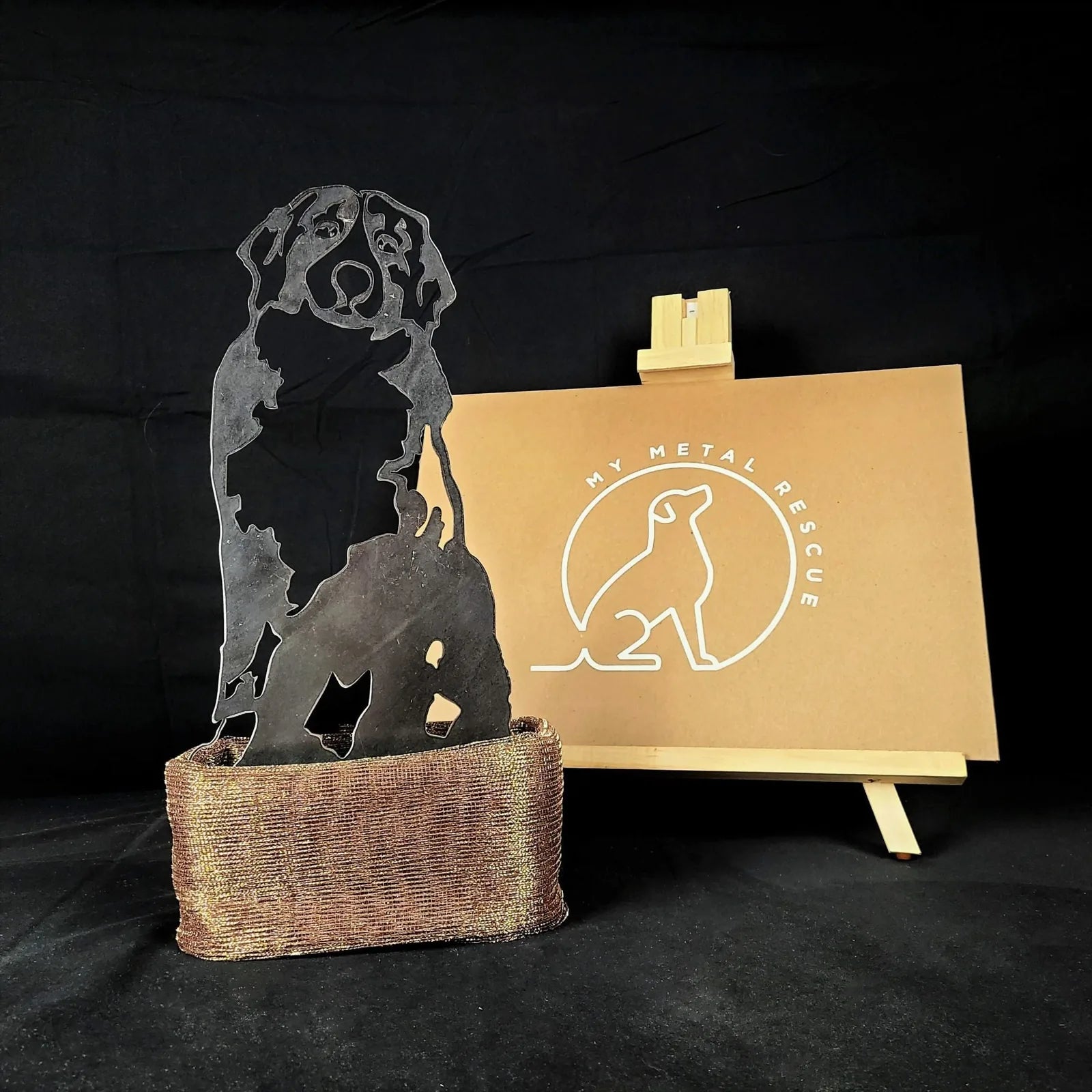 Handmade metal silhouette of a Bernese Mountain Dog in Corten steel with a rust patina, set on a textured base.