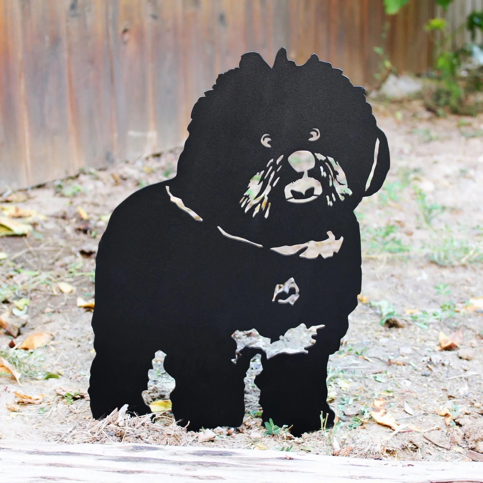 Black metal silhouette of a Bichon Frise dog, showcasing detailed cutouts, set in a garden backdrop.