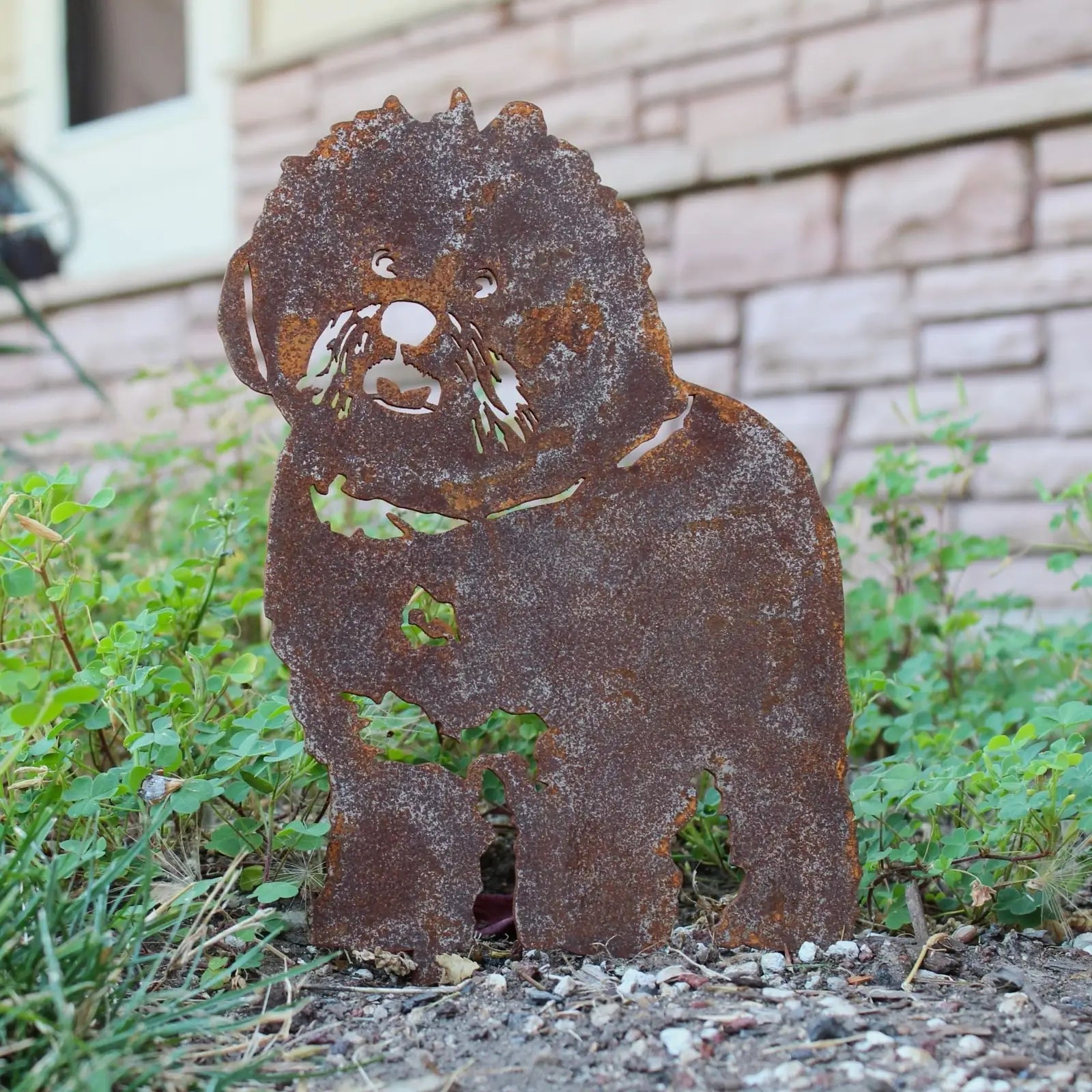 Rusty Corten steel silhouette of a Bichon Frise, set in greenery, showcasing its detailed features and playful stance.