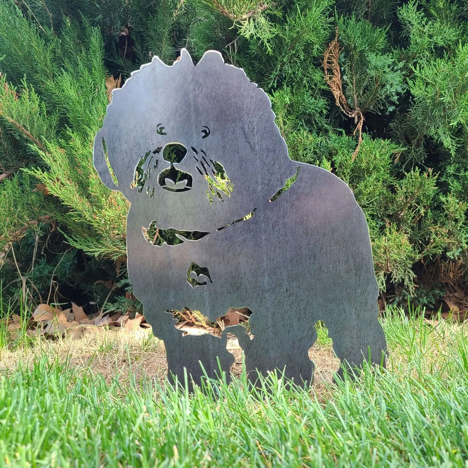 Handcrafted metal silhouette of a Bichon Frise in Corten steel, showcasing its playful form against lush greenery.