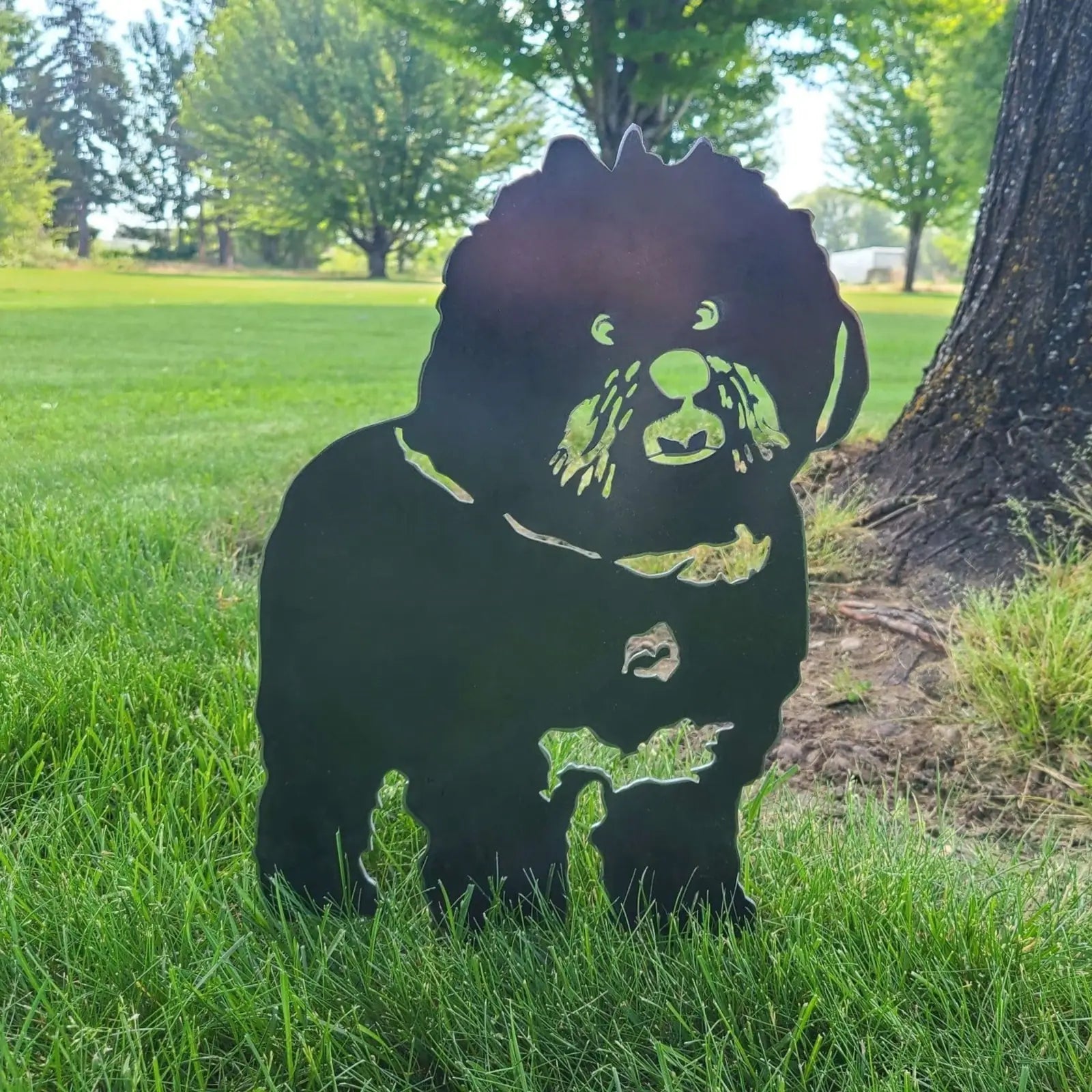 Bichon Frise silhouette in matte black metal, set in green grass with trees in the background, showcasing an elegant design.