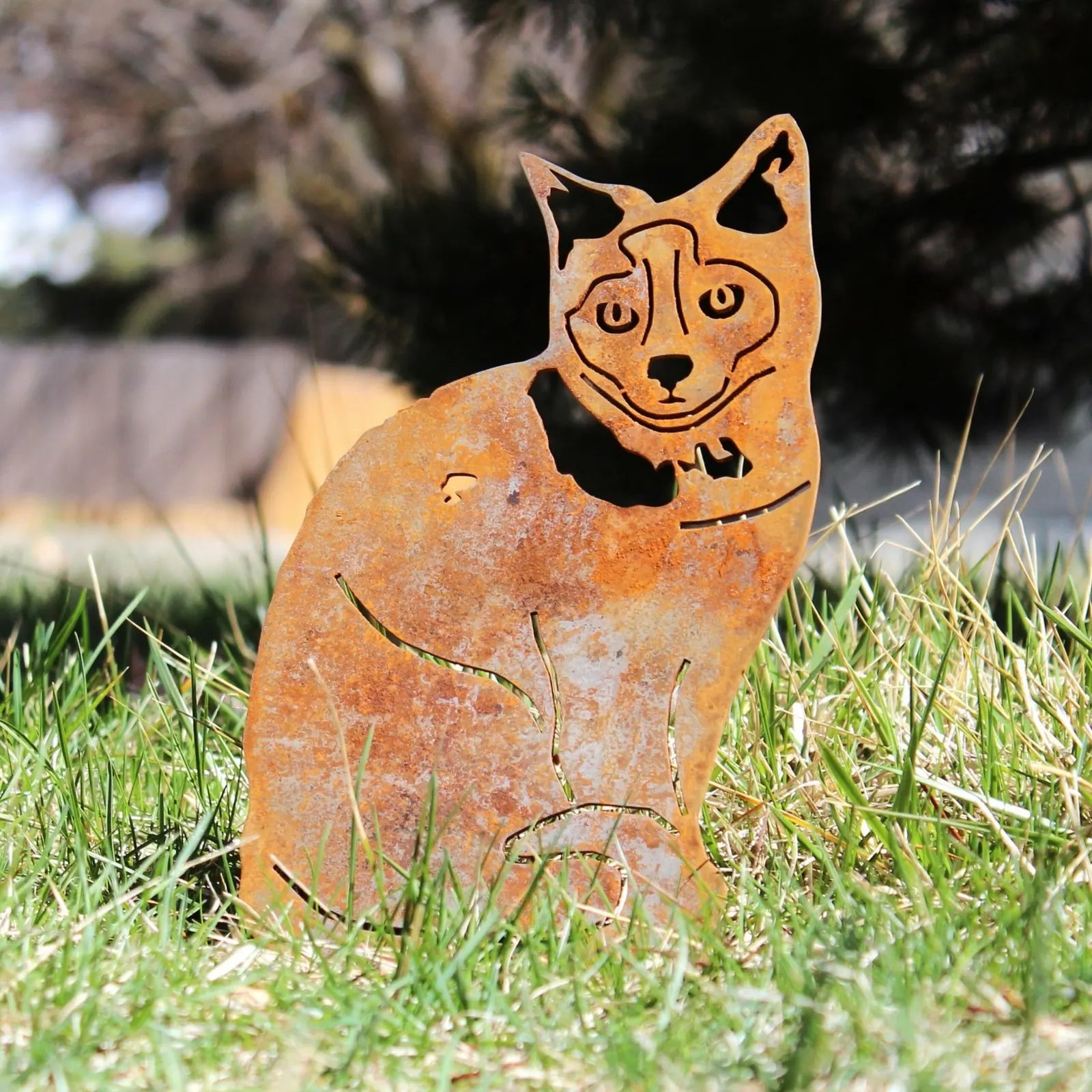 Rusty Corten steel silhouette of a Birman cat, standing in green grass with a clear sky in the background.