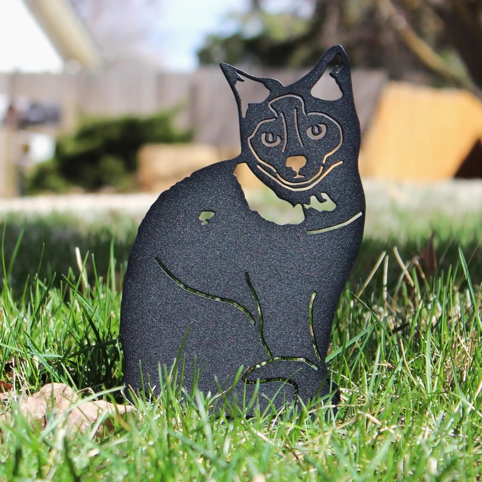 Black metal silhouette of a Birman cat, poised on green grass with a blurred background, perfect for outdoor art.