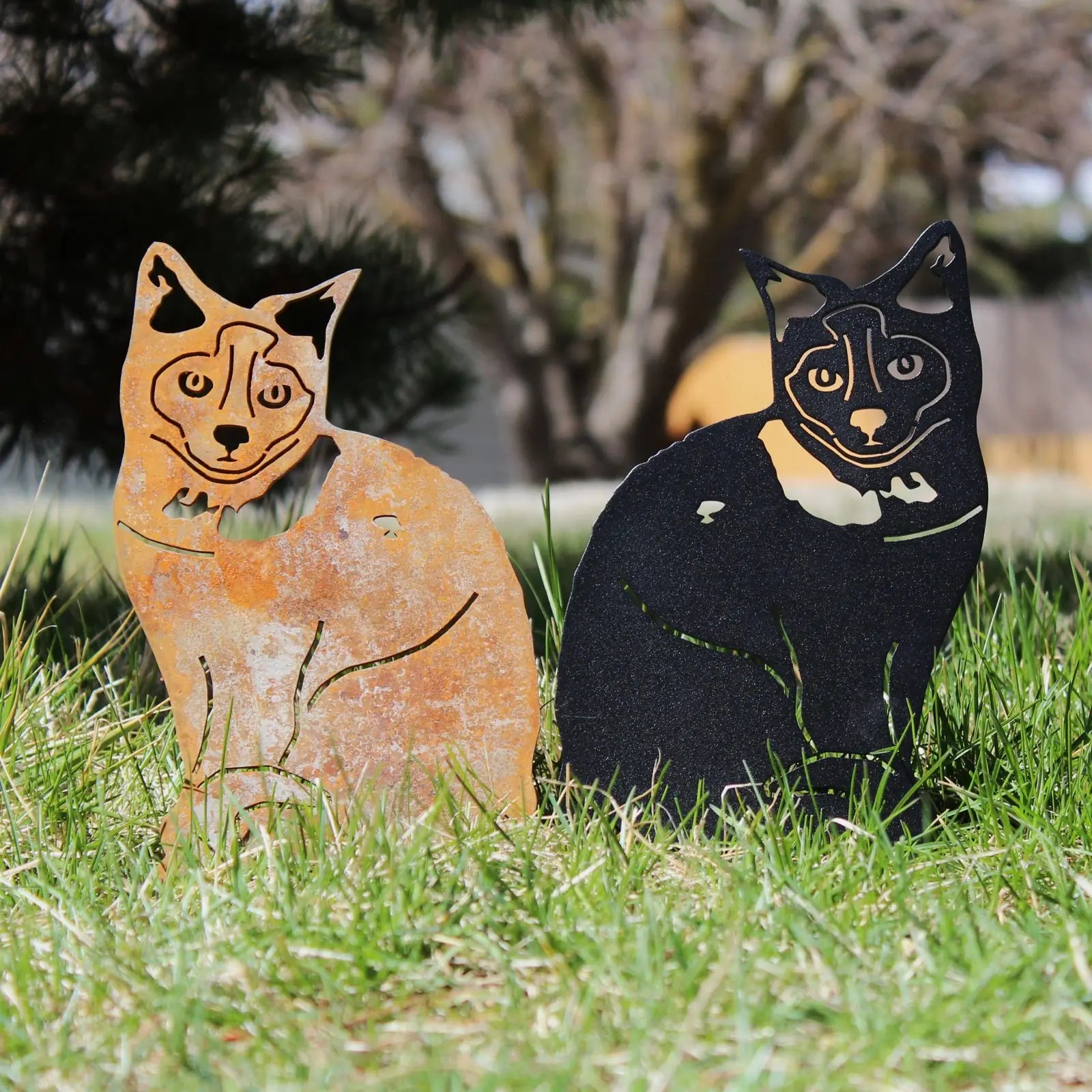 Birman metal silhouette in rusty Corten steel and smooth black finish, surrounded by green grass outdoors.