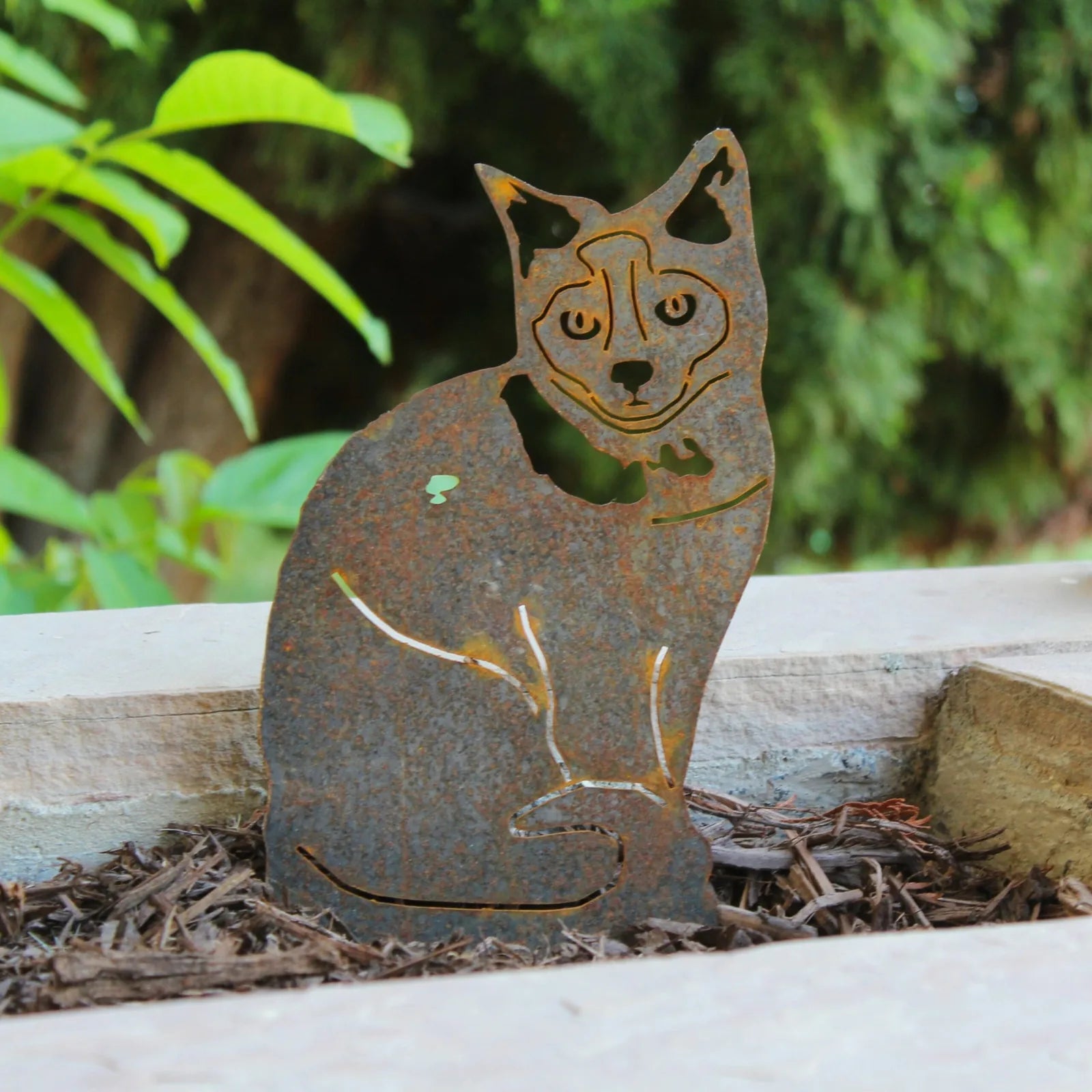 Corten steel Birman dog silhouette with intricate cutouts, resting on mulch among greenery.