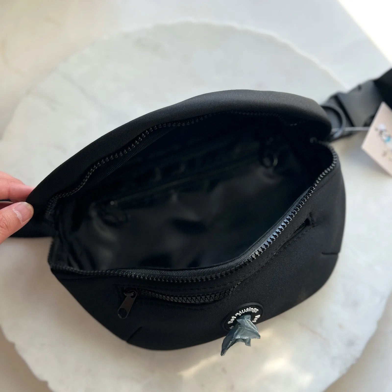 Zippered black dog walking bag featuring a spacious interior, adjustable strap, and a playful charm detail.